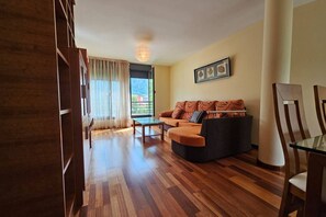 A living room with a sofa, a coffee table, and a chair. There is a window with curtains and a door leading outside. - The Llaneces Lookout 24A02 by R2R Consulting (Arenas de Cabrales)