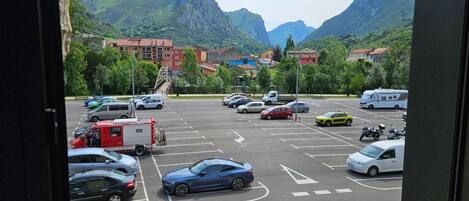A parking lot with cars and a camper, surrounded by buildings and mountains.