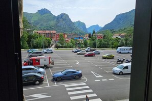 Ein Parkplatz mit Autos und einem Wohnmobil, umgeben von Gebäuden und Bergen.