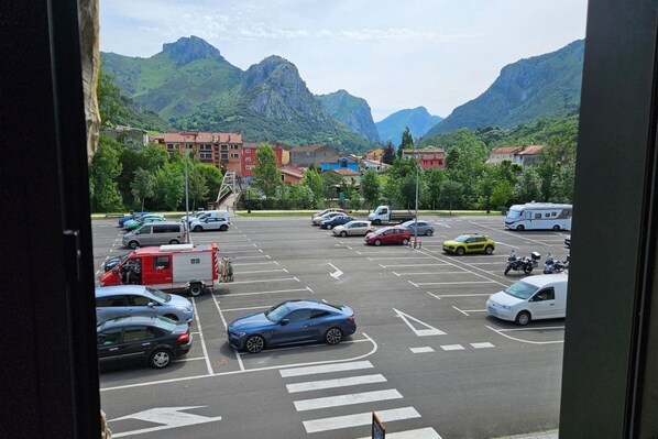 A parking lot with cars and a camper, surrounded by buildings and mountains.
