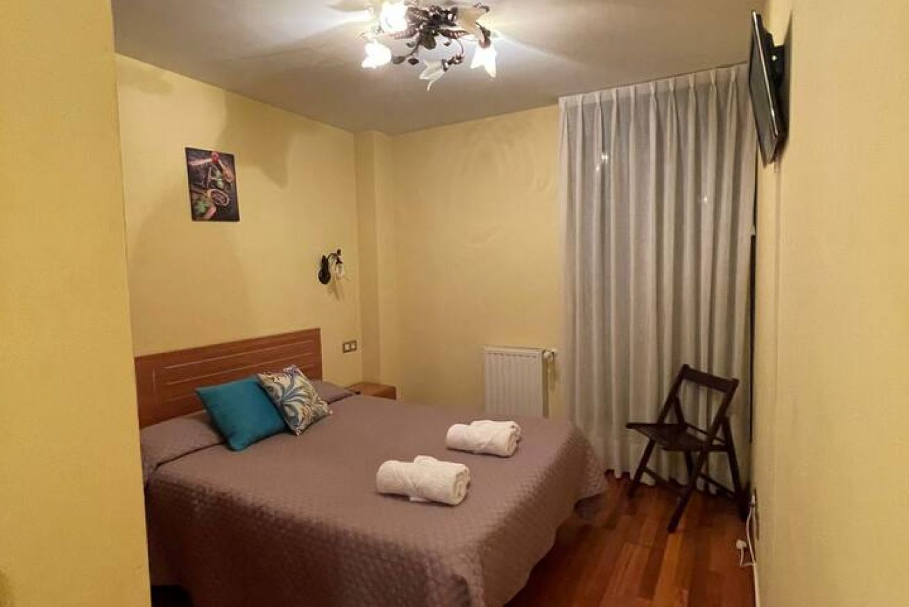 A hotel room with a bed, a chair, a radiator, and a television mounted on the wall.