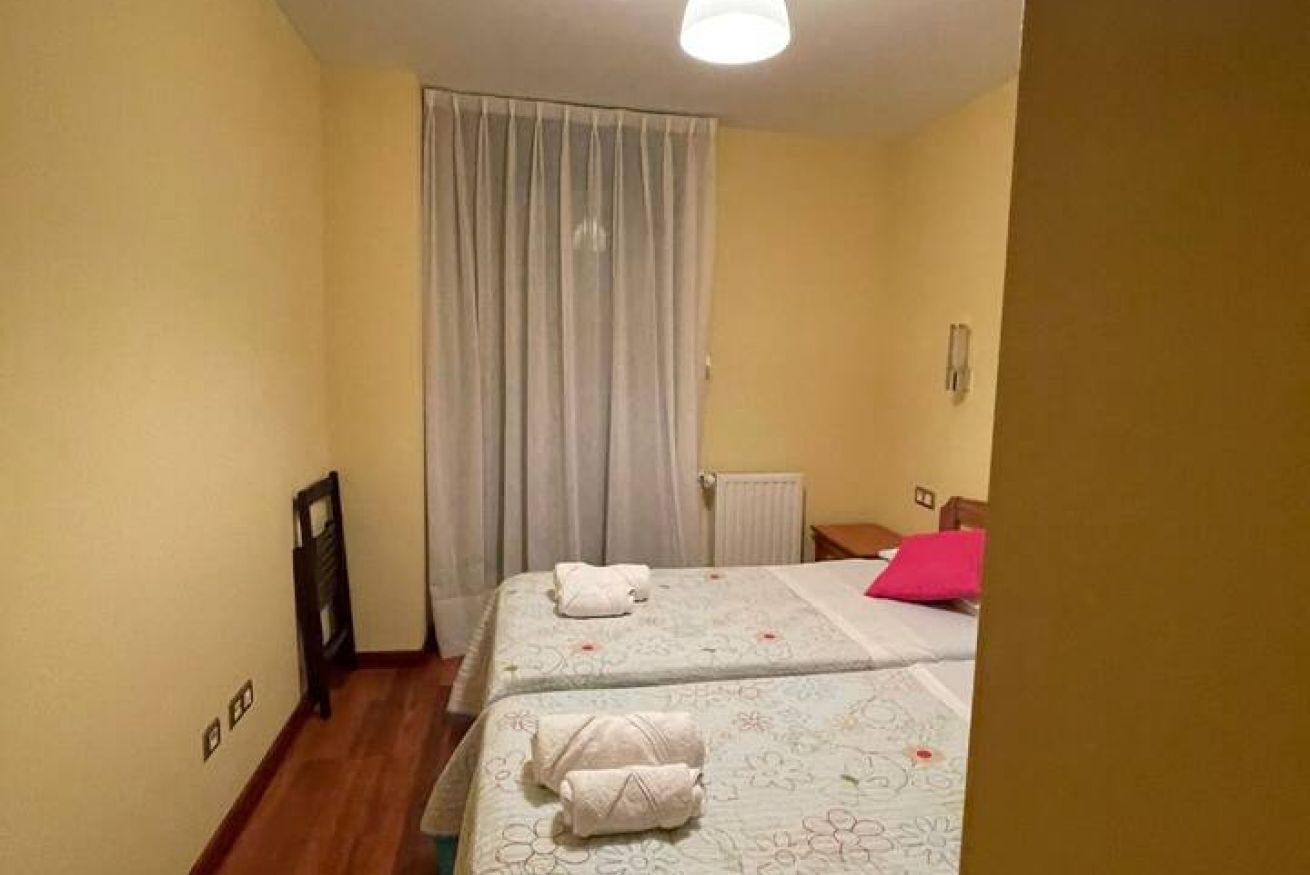 Un dormitorio con dos camas, un radiador, una ventana con cortinas y suelo de madera.
