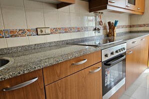 A kitchen with wooden cabinets, a granite countertop, a built-in oven, and a backsplash with patterned tiles. - The Llaneces Lookout 24A02 by R2R Consulting (Arenas de Cabrales)