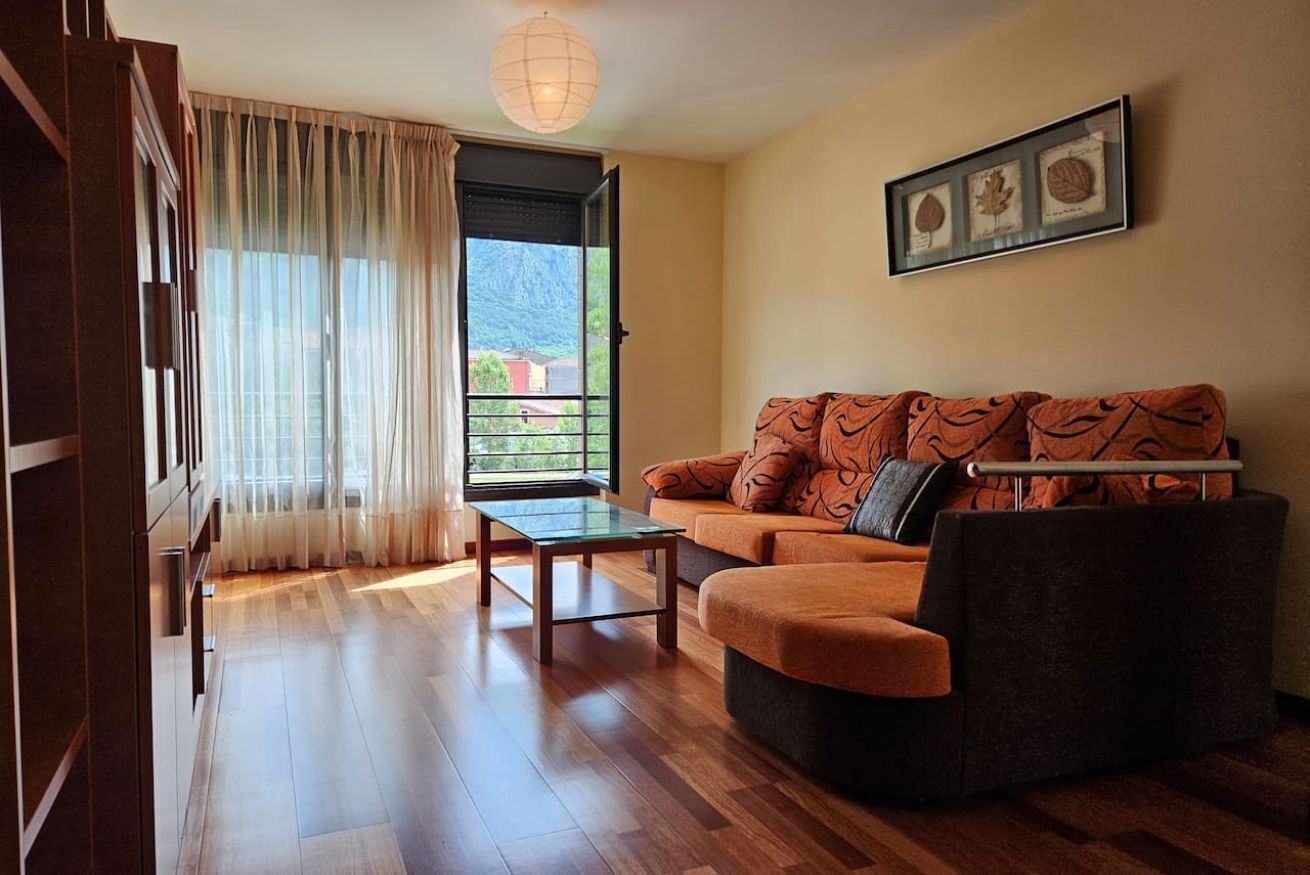 A living room with a sofa, a glass coffee table, a view through a door, and a framed botanical print on the wall.