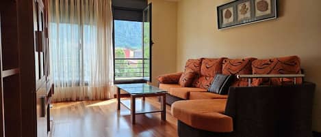 A living room with a sofa, a glass coffee table, a view through a door, and a framed botanical print on the wall.