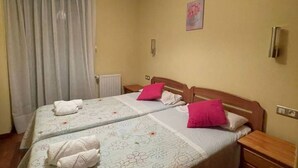 A room with two beds, each with a wooden headboard, white bedding, and pink pillows. There is a window with curtains, a wall-mounted light switch, and a small painting. - The Llaneces Lookout 24A02 by R2R Consulting (Arenas de Cabrales)