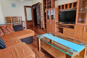 A living room with a glass-top coffee table, wooden cabinets, a television, and a sofa.