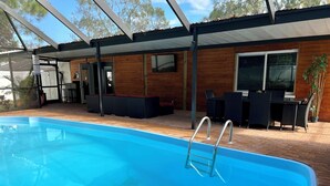 A swimming pool with a metal ladder, surrounded by wooden deck and outdoor furniture. - Unique space with lots of details! (Seffner)