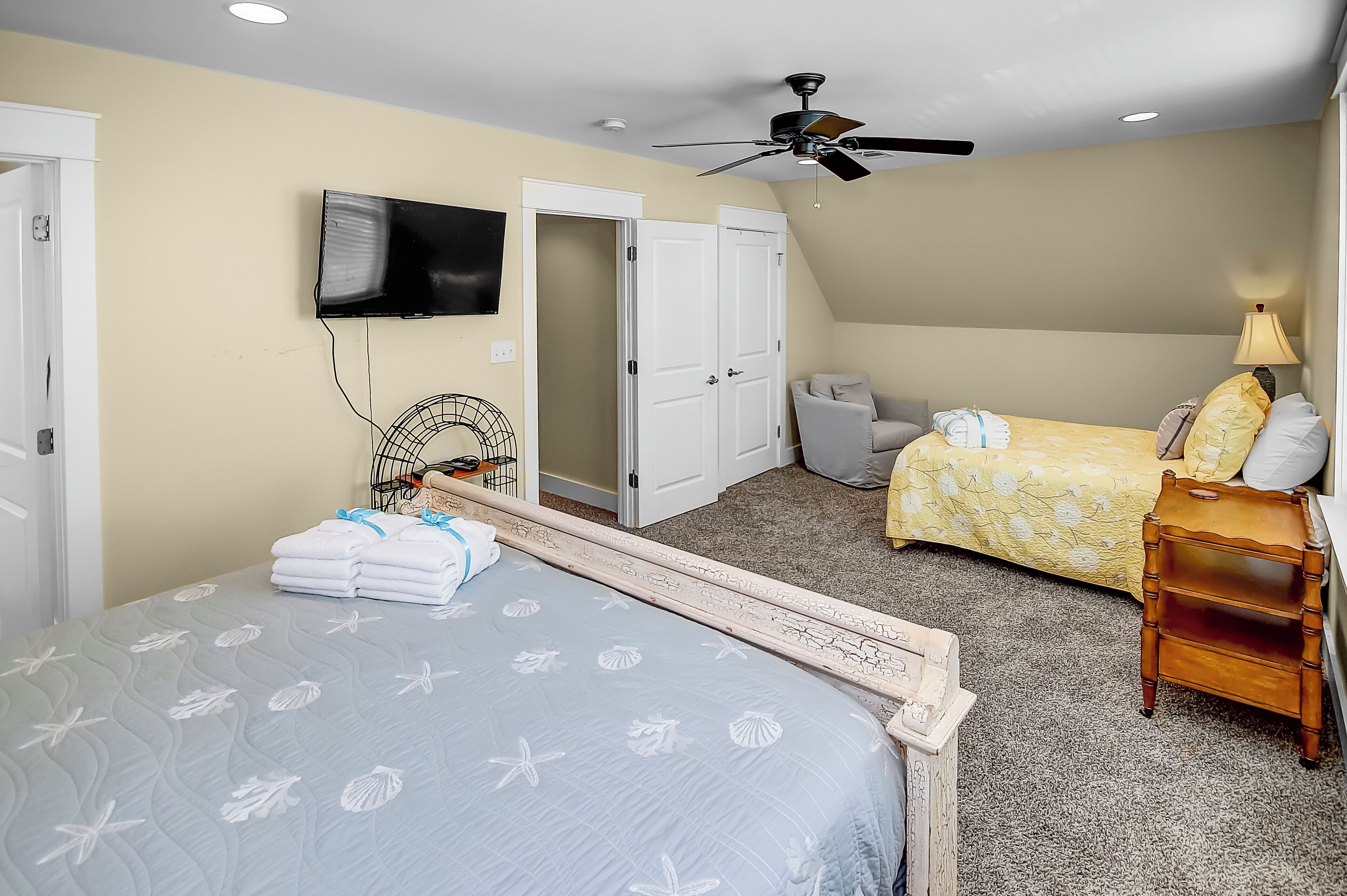 Une chambre avec deux lits, un ventilateur de plafond, une télévision et une lampe.