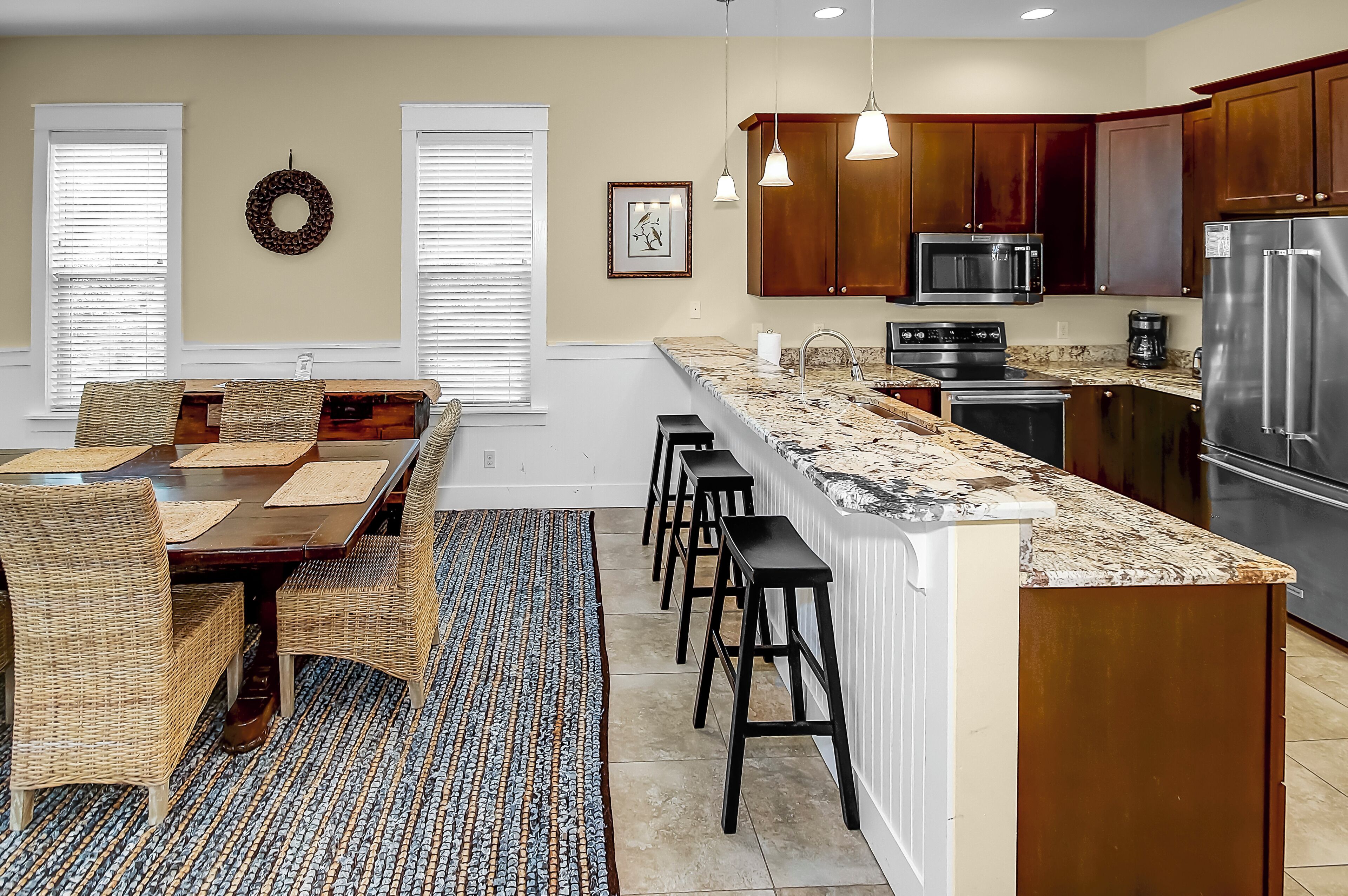 Cocina moderna con una isla grande, armarios de madera, electrodomésticos de acero inoxidable y un comedor con sillas de mimbre y alfombra estampada.