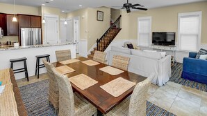 Una cocina moderna con un refrigerador de acero inoxidable, un comedor con mesa de madera y sillas de mimbre, un sofá blanco y un sofá azul.