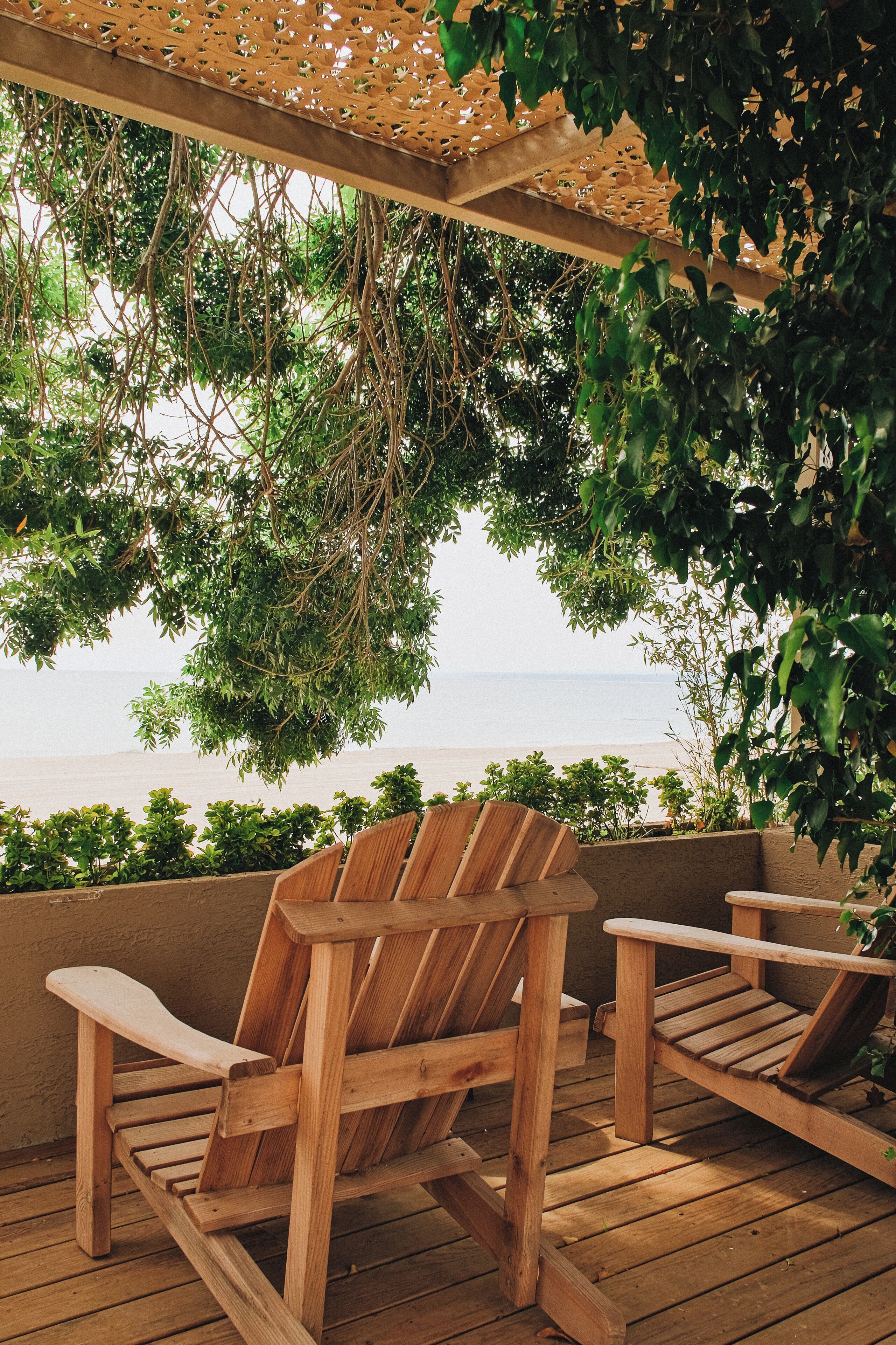 Una terraza de madera con dos sillas Adirondack con vista a la playa.
