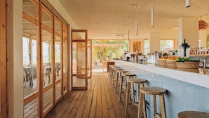 A bar area with wooden stools, a counter with bar tools, and a view of the outdoors. - Nayu Igneada (Demirköy)