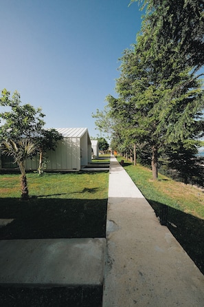 A pathway leading to a white building with a sloped roof, surrounded by trees and grass.