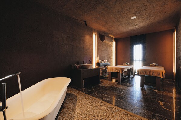 Habitación de spa con bañera, camilla de masaje y una mesita con un cuenco.