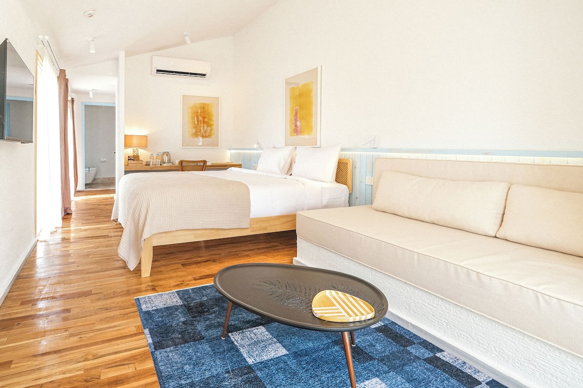 A modern hotel room with a bed, sofa, and a small table.