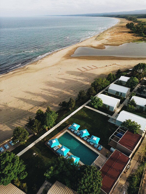 An aerial view of a beachside resort with a swimming pool, umbrellas, and beach access.