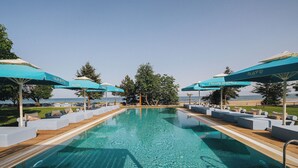 A swimming pool with clear water, surrounded by lounge chairs and umbrellas, with a view of the sea. - Nayu Igneada (Demirköy)