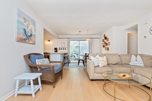 Un salon moderne comprenant un canapé, un fauteuil en osier, une table basse en verre et un coin repas avec une table et des chaises.