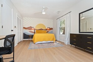 A bedroom with a bed, a desk, a chair, a dresser, and a ceiling fan.