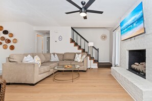 Un salon avec un canapé beige, une table basse en verre, une cheminée et un escalier.