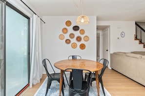 Un coin repas avec une table et des chaises en bois, un luminaire suspendu et un mur décoré d’objets tissés.