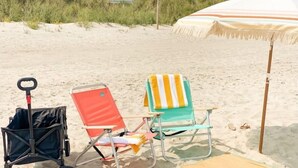 Escena de playa con un cochecito, dos sillas de playa y una sombrilla.