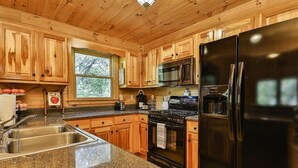 Une cuisine avec des meubles en bois, des plans de travail en granit, un réfrigérateur noir, une cuisinière et un four à micro-ondes.