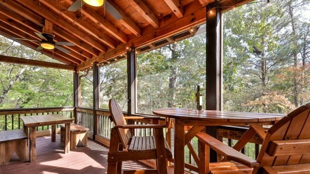 Une terrasse en bois avec une table et des chaises, de grandes fenêtres et un ventilateur de plafond.