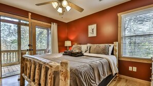 Une chambre avec un lit en bois, un ventilateur de plafond et une grande fenêtre équipée de stores.