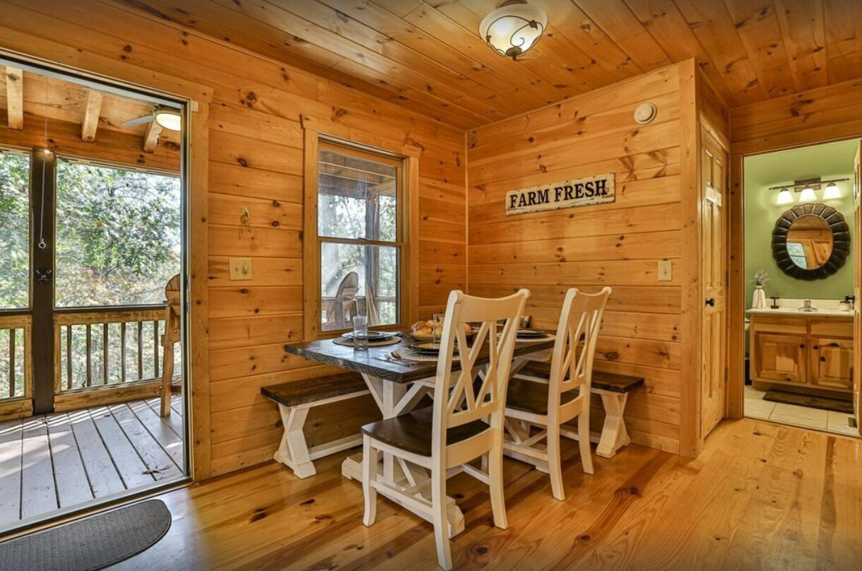 Een houten chalet van binnen, met een eettafel en stoelen, een bordje 'Farm Fresh' en een uitzicht door een raam.