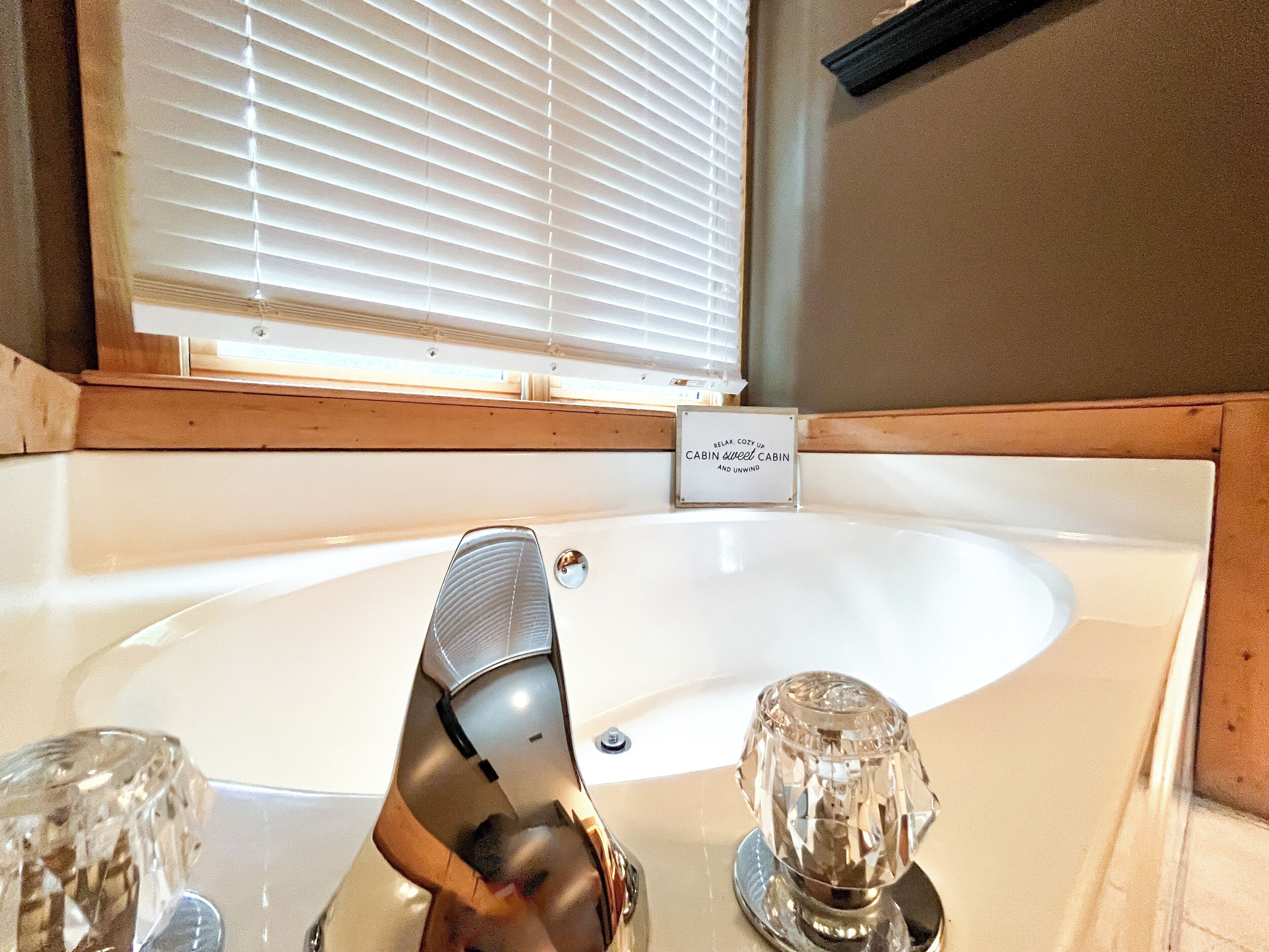 A bathroom with a white bathtub, a glass shower enclosure, and a sign that reads "Relax, Cozy Up Cabin Sweet Cabin and Unwind."