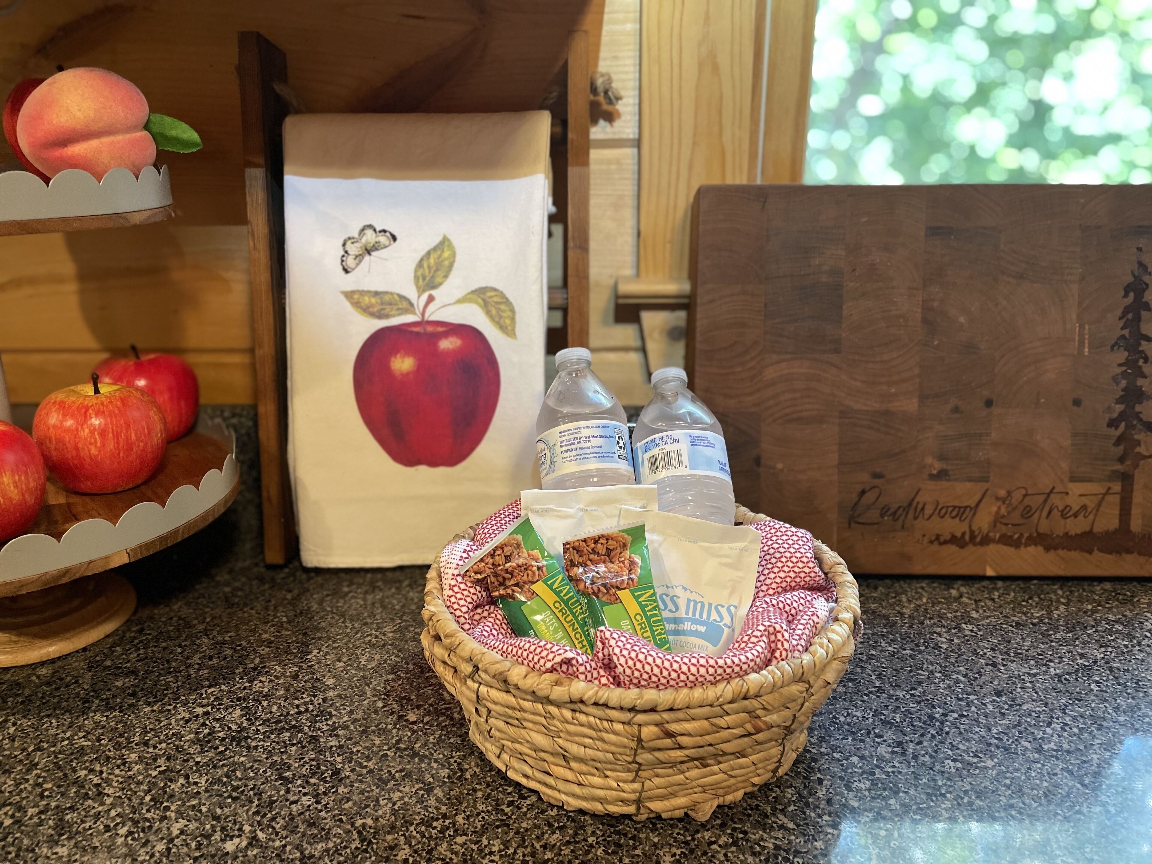 A kitchen counter with a fruit display, a basket of snacks, and a wooden cutting board.