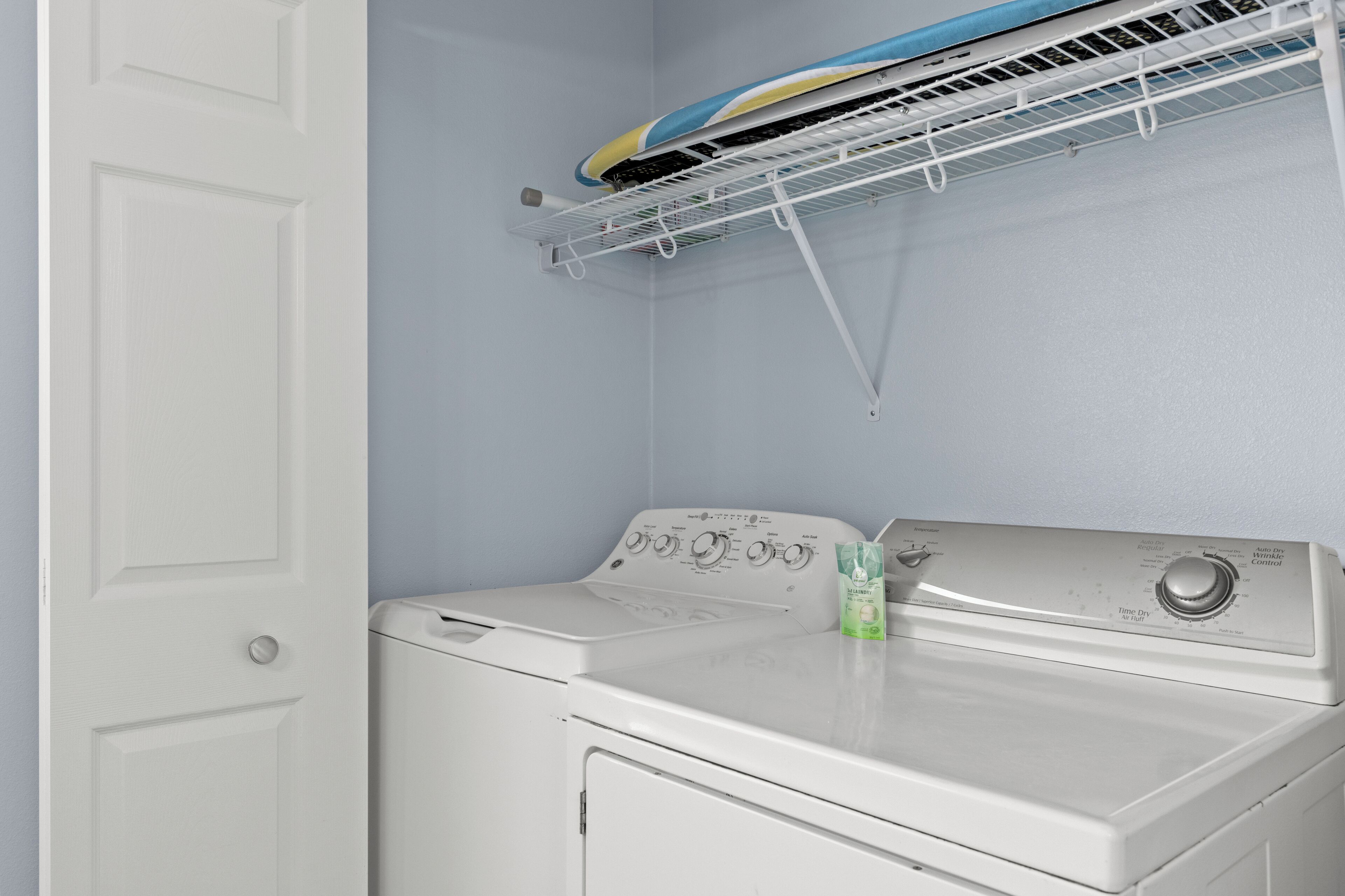 A laundry room with a washing machine and dryer, a drying rack above the dryer, and a door to the left.