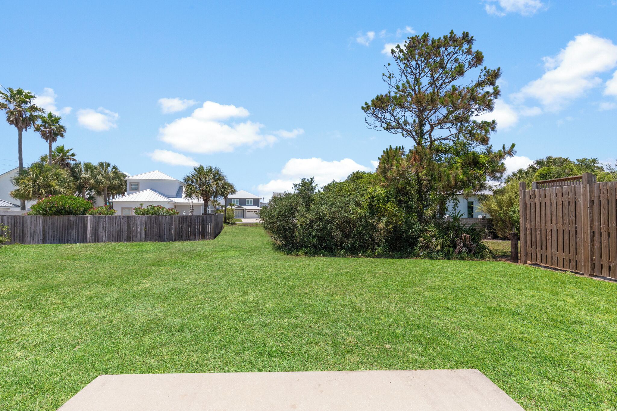 A backyard with a wooden fence, a concrete patio, and a lawn.