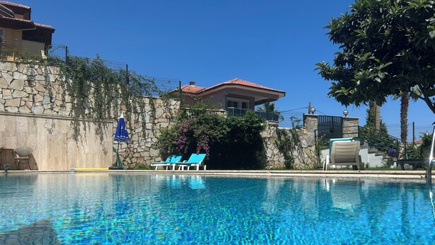 A swimming pool with clear water, lounge chairs, and a stone wall with greenery. - White Suites Icmeler (Marmaris)