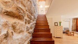 Una escalera con un muro de piedra a un lado y un piso de madera al otro, que conduce a una habitación con un sofá y una mesita.