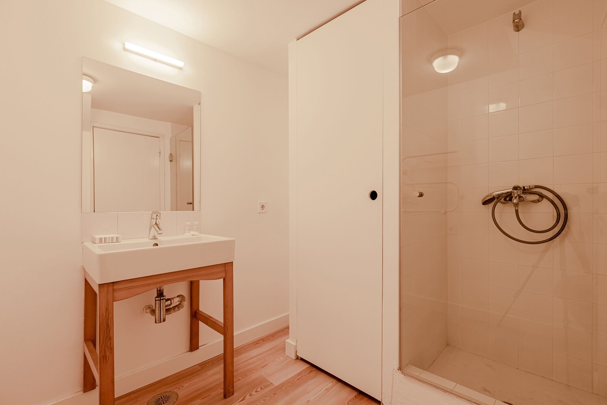 Een badkamer met een wit wastafel, spiegel en douche.