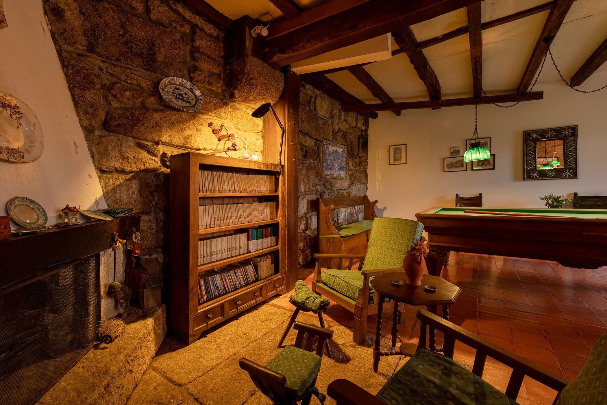 Een gezellige kamer met een stenen muur, houten boekenkasten, een open haard, een biljarttafel en comfortabele zitplaatsen.