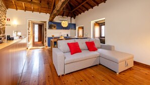 Un salón amplio con techo de madera, un sofá gris con cojines rojos, y una cocina al fondo.