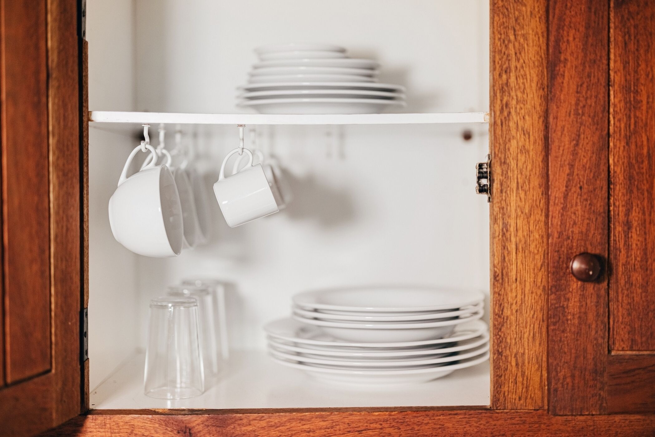 A kitchen cabinet with white plates and cups hanging from hooks.