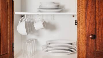 A kitchen cabinet with white plates and cups hanging from hooks.