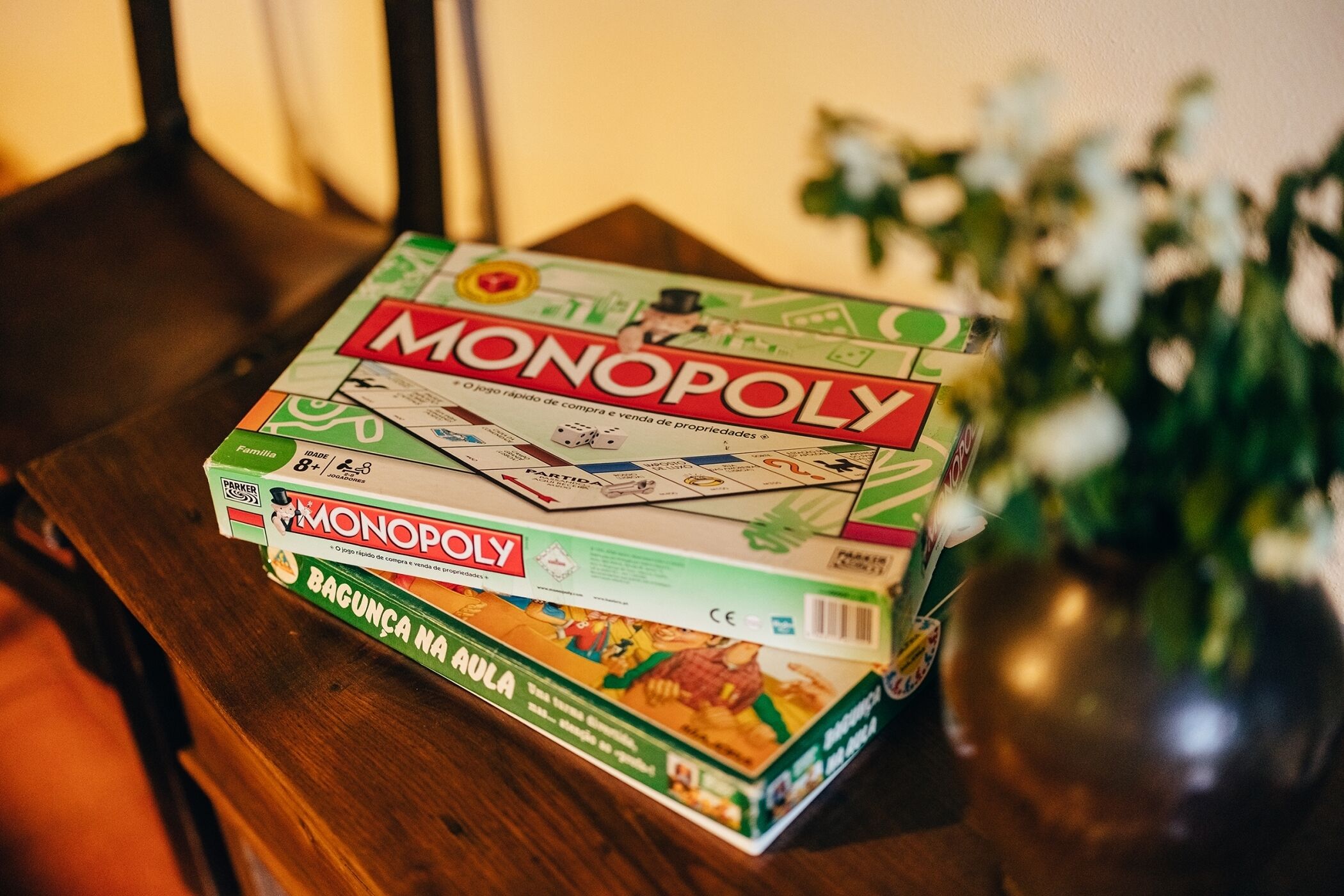A Monopoly board game on a wooden table with a vase of flowers in the background.