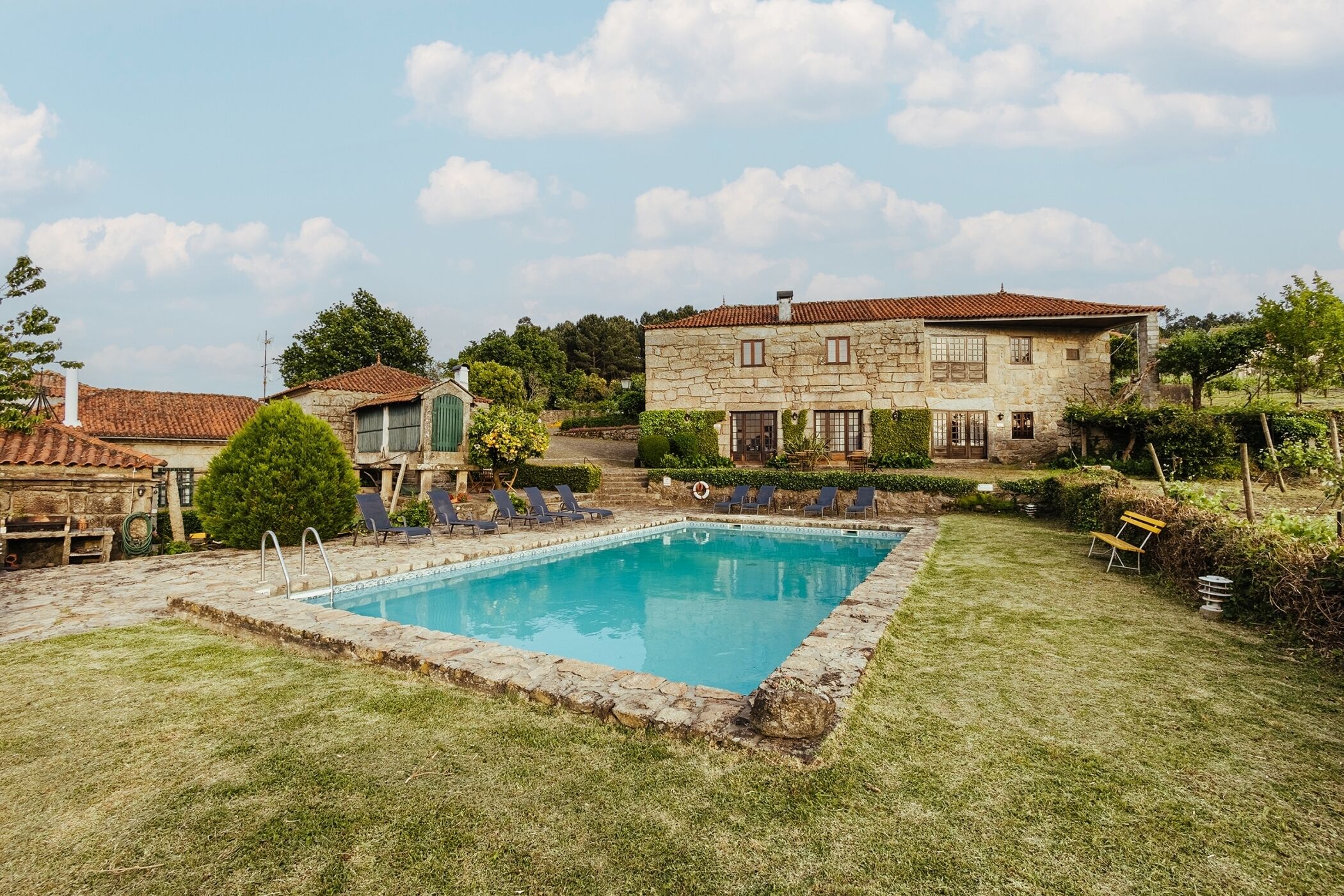 A swimming pool surrounded by a stone deck, with lounge chairs and a stone building in the background.