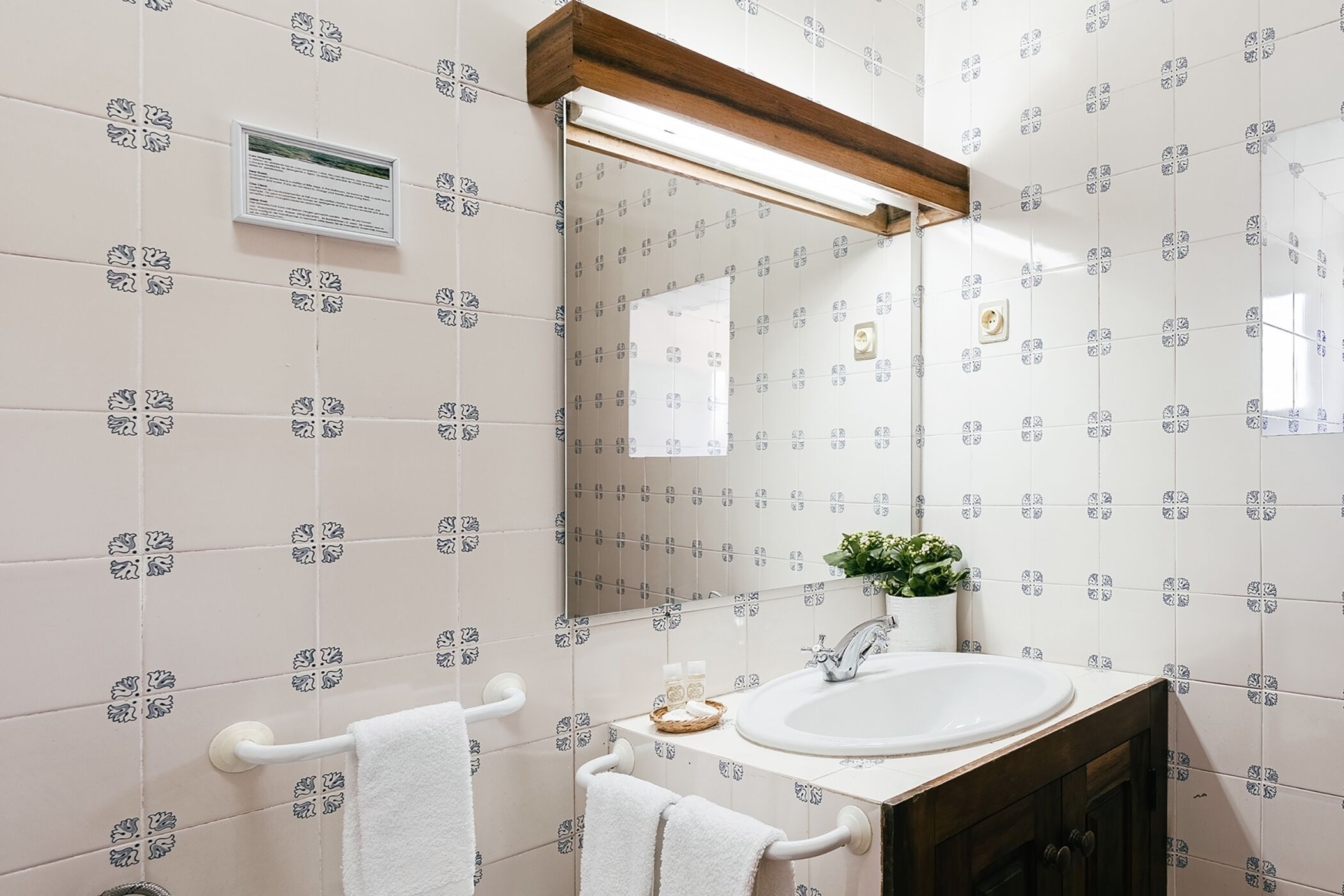 Un baño con azulejos blancos, un lavamanos blanco, un espejo y un perchero para toallas.