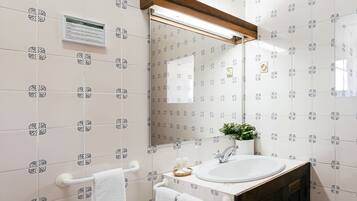 Un baño con azulejos blancos, un lavamanos blanco, un espejo y un perchero para toallas.