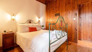 Una habitación con paneles de madera, una estructura de cama metálica, ropa de cama blanca y dos lámparas fijadas a la pared.
