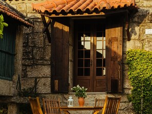 A stone building with a wooden door and shutters, a tiled roof, and a table with chairs outside. - Quinta Stº António | Casa do Padeiro | Monção | Rural Tourism | Pool (Monção)