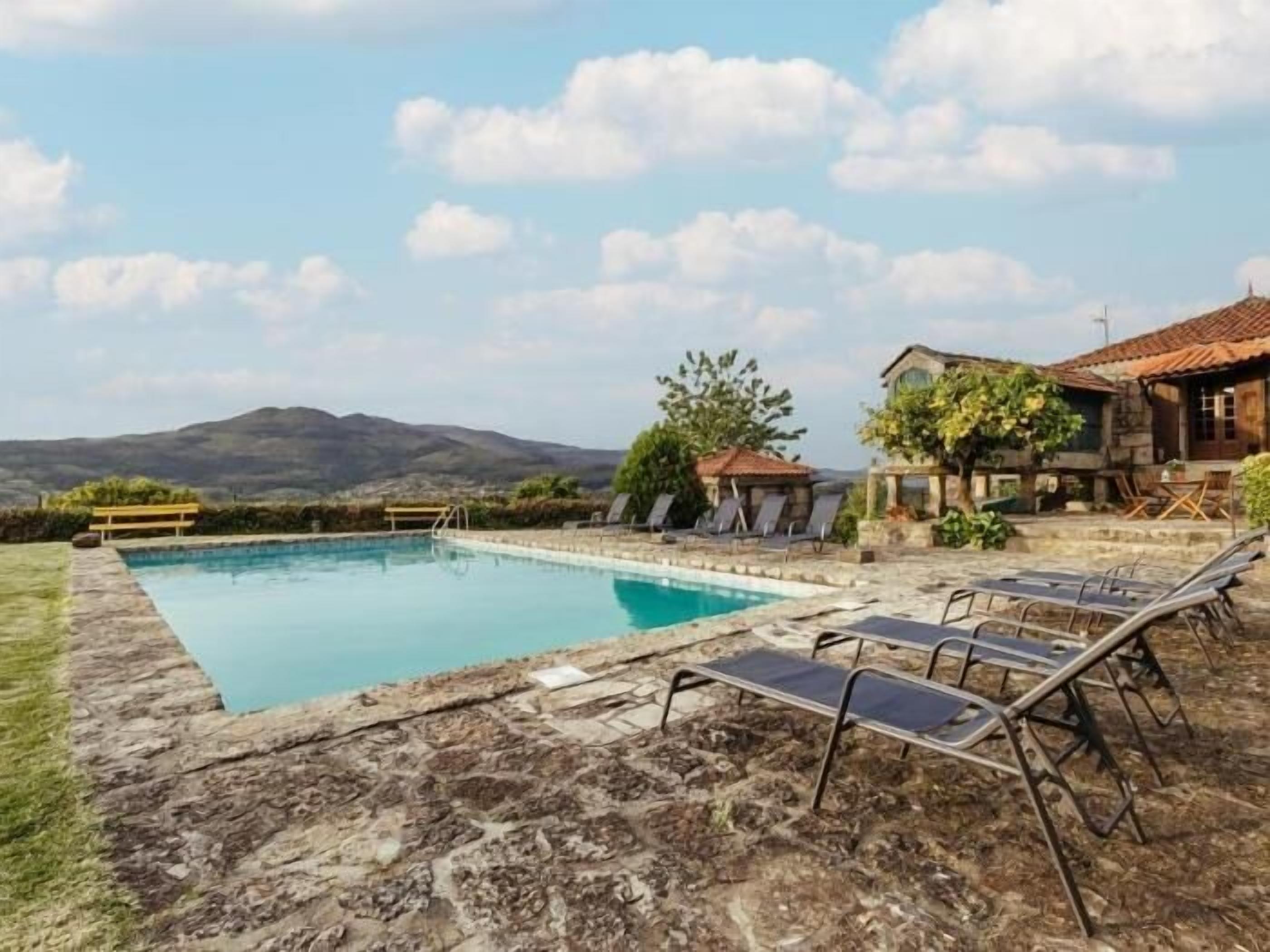 Una piscina con lettini, un solarium in pietra e vista sulle montagne.