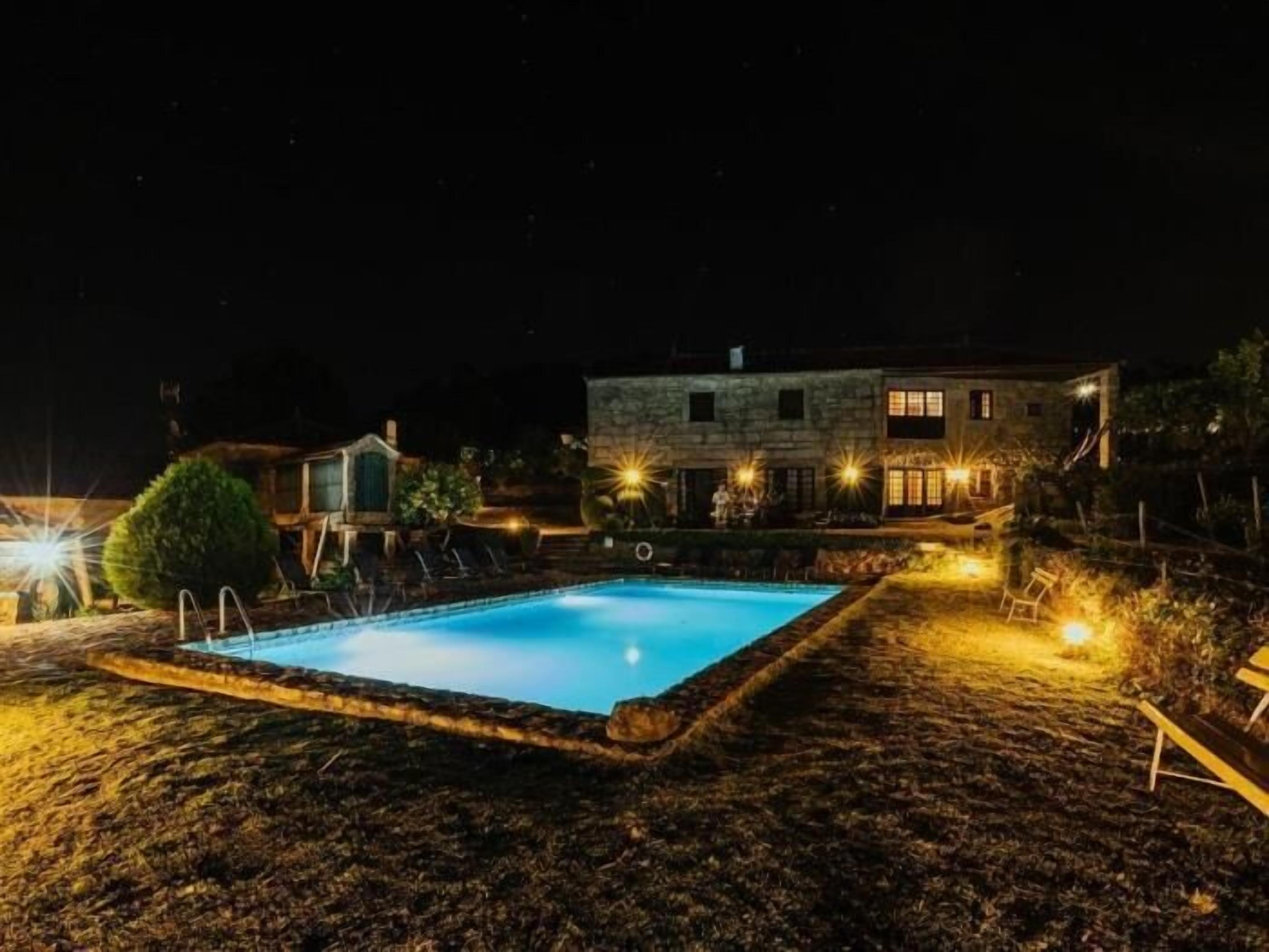 Una casa de piedra con piscina por la noche, rodeada de un jardín ajardinado.